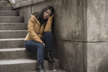 Çekici, üzgün ve depresif, kışlık ceketli Çinli bir kadın sokak köşesindeki merdivenlerde oturuyor. Depresyonda, çaresiz hissediyor.