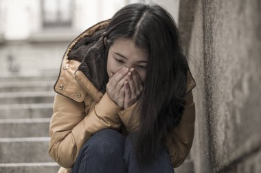 Çekici, üzgün ve depresif, kışlık ceketli Çinli bir kadın sokak köşesindeki merdivenlerde oturuyor. Depresyonda, çaresiz hissediyor.
