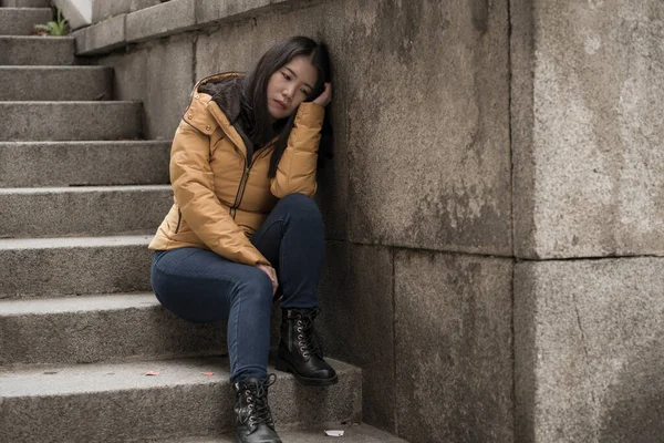 Çekici, üzgün ve depresif, kışlık ceketli Çinli bir kadın sokak köşesindeki merdivenlerde oturuyor. Depresyonda, çaresiz hissediyor.