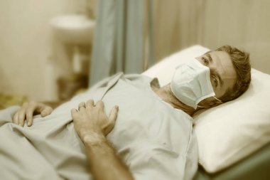 Çekici ve korkmuş bir adamın sanatsal portresi. Kovid 19 tarafından enfekte edilmiş. Klinikte yüz maskesi takmış yetişkin bir erkek.