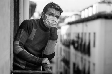 Coronavirus dramatik karmaşası - Yüzü maskeli çekici bir adamın evde karantina portresi Hüzünlü ve depresif bir şekilde ev balkonunda