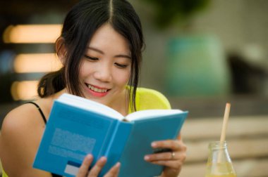 Çekici bir Asyalı kadın kitap okuyor. Genç, güzel ve mutlu bir Koreli kızın roman okuduğu ya da açık hava kahve dükkanında rahatlamış portakal suyu içtiği bir resim.