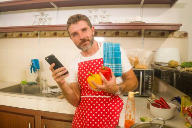 İşte ev aşçısı. Kırmızı önlüklü genç ve çekici aşçı. İnternette cep telefonu tarifini takip ediyor.