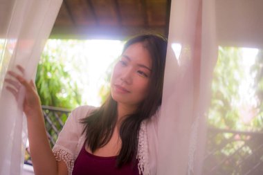 Lüks otel odasının balkonunda rahat ve keyifli tatil ve seyahat kavramının tadını çıkaran mutlu ve güzel Asyalı kadının arka ışıklandırılmış hayali portresi.