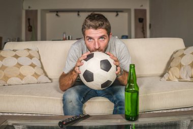 Futbolcu destekçisi televizyondaki maçtan zevk alıyor. Sinirli ve çekici bir futbol fanatiği, televizyon seyrediyor. Kanepede kanepe izliyor. Spor duyguları konseptinde bira şişesi içiyor.