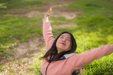 Mutlu ve güzel Asyalı pembe kazaklı genç bir kadının hayat tarzı portresi yeşil çimenlerin üzerinde uzanmış neşeli ve heyecanlı bir şekilde dışarıda eğleniyor kaygısızca eğleniyor.