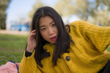 Şehir parkındaki güzel Asyalı kadın. Genç, güzel ve mutlu bir Japon kızın portresi. Yeşil çimlerde oturuyor. 