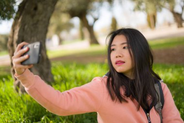 Şehir parkındaki genç mutlu Asyalı kadın. Neşeli ve güzel Çinli kızın portresi. Cep telefonuyla selfie çekiyor. 