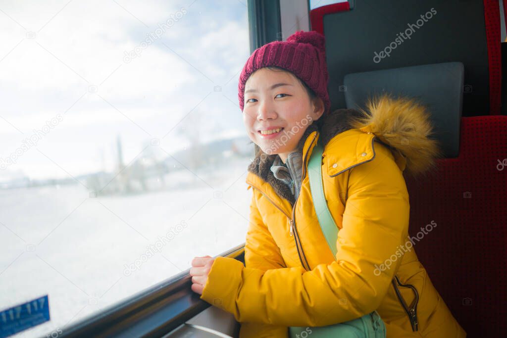 train travel getaway - young happy and beautiful Asian Chinese woman enjoying snow landscape through railcar window during Winter holiday tri