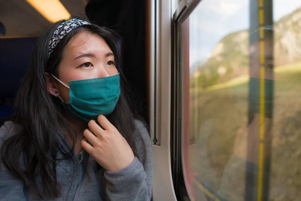 train travel in times of covid19 - young happy and cute Asian Chinese woman in  face mask traveling on railcar enjoying landscape through the window