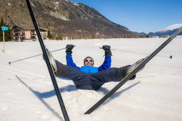 lifestyle portrait of young happy and funny man in cross country ski lying on snow playful enjoying winter holidays on Swiss Alps having fun