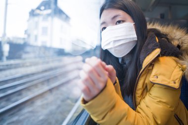 Güzel ve düşünceli Asyalı Çinli bir kadının hayat tarzı portresi. Yüz maskesi takmış bir Çinli kadın. Tren yolculuğu sırasında pencereden dışarı bakıyor.