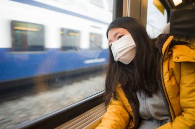 Güzel ve düşünceli Asyalı Japon kadının hayat tarzı portresi. Yüz maskesi takan Japon kadın. Tren yolculuğu sırasında pencereden dışarı bakıyor.