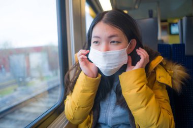 Güzel ve düşünceli Asyalı Japon kadının hayat tarzı portresi. Yüz maskesi takan Japon kadın. Tren yolculuğu sırasında pencereden dışarı bakıyor.