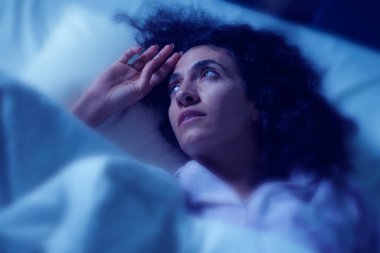 Depresyondaki ve uykusuz Latin kadının karanlık ve gergin portresi. Endişeli ve uyanık bir şekilde yatarken uykusuzluk ve depresyon sorunu yaşıyor.
