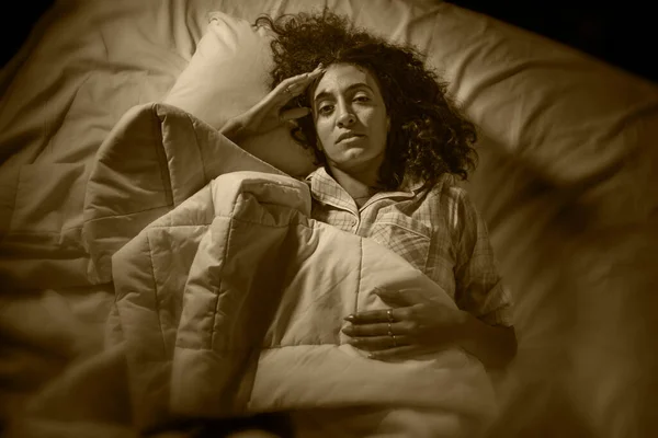 dark and edgy portrait of depressed and sleepless latin woman lying worried and awake on bed at night suffering insomnia and depression problem