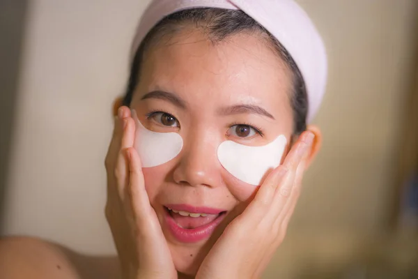 美丽的亚裔韩裔女性在浴室镜子前使用抗熊猫眼罩进行皮肤护理和美容治疗的肖像 — 图库照片