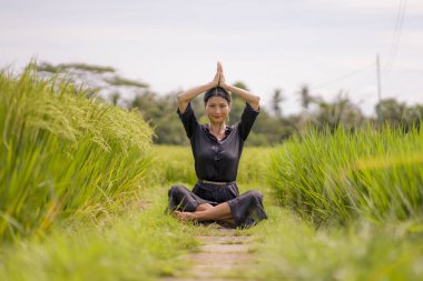 Çekici ve mutlu Asyalı bir kadının sanatsal portresi yeşil pirinç tarlasında dans ediyor ve yoga gevşeme egzersizi yapıyor ve meditasyon yapıyor. 