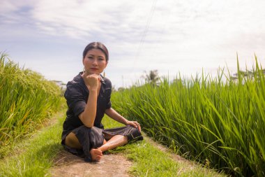 Çekici ve mutlu Asyalı bir kadının sanatsal portresi yeşil pirinç tarlasında dans ediyor ve yoga gevşeme egzersizi yapıyor ve meditasyon yapıyor. 