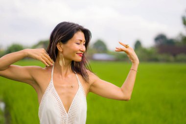 Çekici ve mutlu Asyalı kadının sanatsal portresi yeşil pirinç tarlasında zarif uzun elbiseler içinde tasasız bir şekilde dans ediyor. 