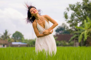 Çekici ve mutlu Asyalı kadının sanatsal portresi yeşil pirinç tarlasında zarif uzun elbiseler içinde tasasız bir şekilde dans ediyor. 