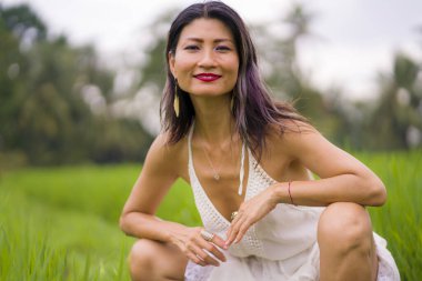 Çekici ve mutlu Asyalı kadının sanatsal portresi yeşil pirinç tarlasında zarif uzun elbiseler giyerek güzel doğanın tadını çıkarıyor. 