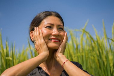 Çekici ve mutlu Asyalı kadının sanatsal portresi yeşil pirinç tarlasında zarif uzun elbiseler giymiş rahat ve tasasız doğanın tadını çıkarıyor.