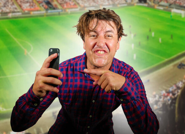 conceptual composite with happy and excited man with mobile phone and soccer background in online sport bet and internet gambling concept winning and making money