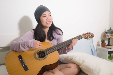 Genç mutlu Asyalı kadın yatakta gitar çalıyor. Yatak odasında çekici ve güzel bir Koreli kız. Evde rahat rahat şarkı söyleyip şarkı yazmaktan zevk alıyor.