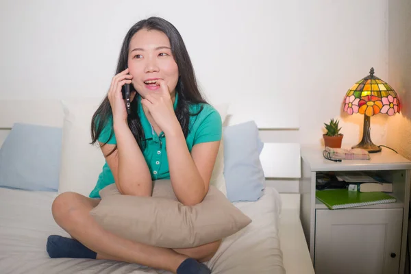 家庭生活ポートレートの若いです幸せと魅力的なアジアの中国人女性に座っていますベッドの上で話す携帯電話とともに彼女のゴシップ陽気でリラックス — ストック写真
