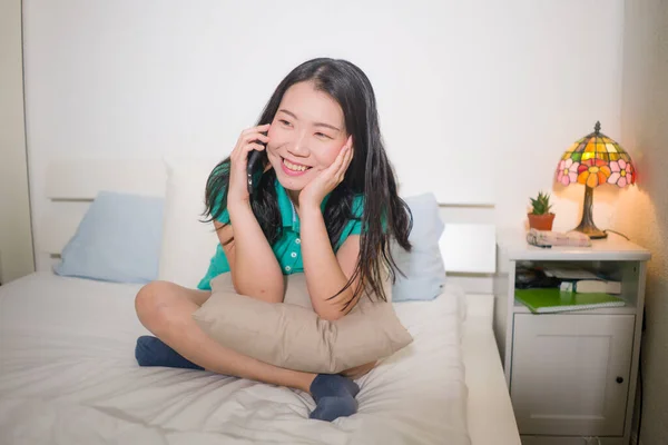 幸せと魅力的な若いアジア系日本人女性のホームライフスタイルのポートレートベッドの上に座っている携帯電話で話している彼女のゴシップ陽気でリラックスした — ストック写真