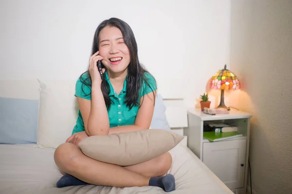 幸せな若いと魅力的なアジアの韓国人女性の家のライフスタイルのポートレートベッドの上で話して座っている携帯電話で彼女のゴシップ笑い陽気でリラックスした — ストック写真