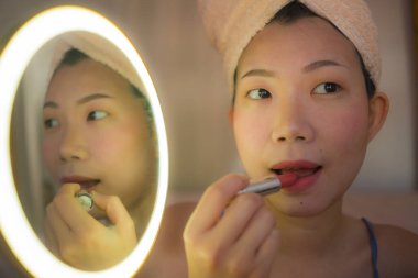 Kırmızı rujlu güzel bir Asyalı kadın. Mutlu ve güzel bir Çinli kızın portresi. Aynaya bakarak makyaj ve yüz güzelliği tedavisi uyguluyor.