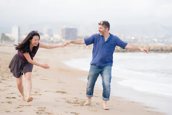 young beautiful and happy mixed ethnicity couple of Asian woman and Caucasian man relaxed and cheerful walking playful  on beach enjoying love and romantic holidays