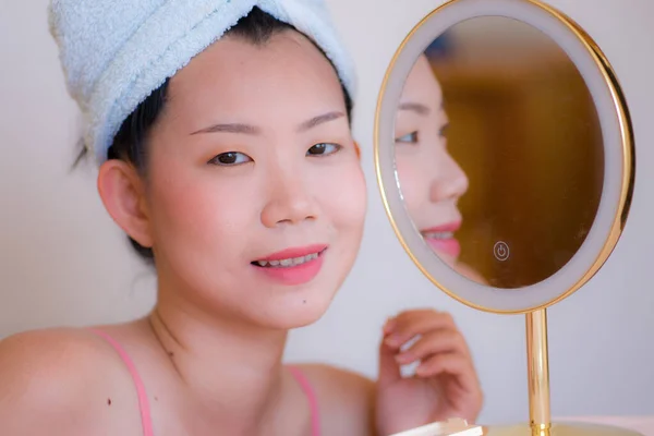 Asian woman and makeup - lifestyle portrait of young beautiful and happy Chinese girl with towel head wrap next to mirror smiling cheerful in beauty and fashion concept
