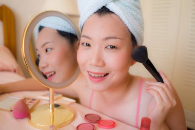 Güzel ve mutlu Asyalı bir Çinli kadın havluyla makyaj yapıyor aynaya bakıp gülümsüyor ve güzellik modasına hazırlanıyor.