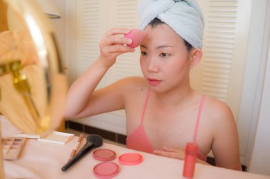Güzel ve mutlu bir Asyalı kadın havluyla makyaj yapıyor aynaya bakıp gülümsüyor ve güzellik modasına hazırlanıyor.
