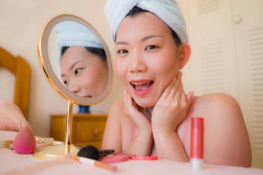 Güzel ve mutlu bir Asyalı kadın havluyla makyaj yapıyor aynaya bakıp gülümsüyor ve güzellik modasına hazırlanıyor.