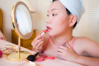 Güzel ve mutlu Asyalı kadın havluyla sarmalayıp makyaj yapıyor aynaya bakıp gülümsüyor ve güzellik modasına hazırlanıyor.