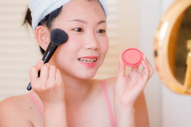 Güzel ve mutlu Asyalı kadın havluyla sarmalayıp makyaj yapıyor aynaya bakıp gülümsüyor ve güzellik modasına hazırlanıyor.