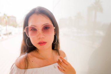 Güzel ve çekici Asyalı bir kadının güzel ve çekici portresi. Güneş gözlüğü takıyor. Güneşli bir günde dışarıda poz veriyor.