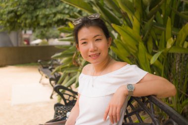 Parktaki bankta oturan genç, güzel ve mutlu Asyalı kadın. Turist yürüyüşü sırasında dinlenen yaz elbiseli çekici Çinli bir kızın portresi. 