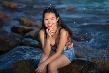 Deniz kenarındaki genç Asyalı kadının tatil tarzı portresi. Mutlu ve güzel Koreli kız plaj gezisinin keyfini çıkarıyor. Plaj kayalıklarında rahat ve neşeli.