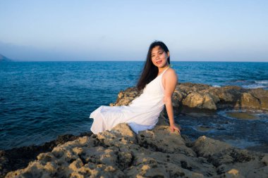 Deniz kenarındaki genç Asyalı kadının tatil tarzı portresi. Mutlu ve güzel Koreli kız plaj gezisinin keyfini çıkarıyor. Plaj kayalıklarında rahat ve neşeli.