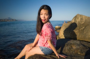 Deniz kenarındaki çekici Koreli kız okyanus manzaralı kayalıklarda tatilin tadını çıkarıyor.