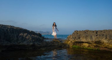 Deniz kenarındaki çekici Koreli kız okyanus manzaralı kayalıklarda tatilin tadını çıkarıyor.