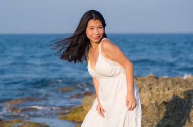 Deniz kenarındaki çekici Koreli kız okyanus manzaralı kayalıklarda tatilin tadını çıkarıyor.