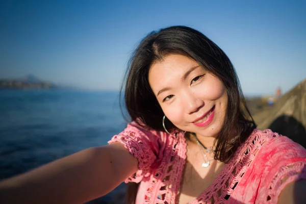 행복하고 아름다운 아시아 소녀와 전화로 셀피를 복용하며 해변에서 편안하게 휴가를 — 스톡 사진