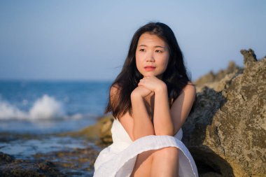 young happy and beautiful Asian woman by the sea - Attractive Chinese girl in white dress enjoying relaxed summer holidays at tropical island in travel and lifestyle concept