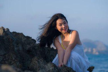 young happy and beautiful Asian woman by the sea - Attractive Japanese girl in white dress enjoying relaxed summer holidays at tropical island in travel and lifestyle concept